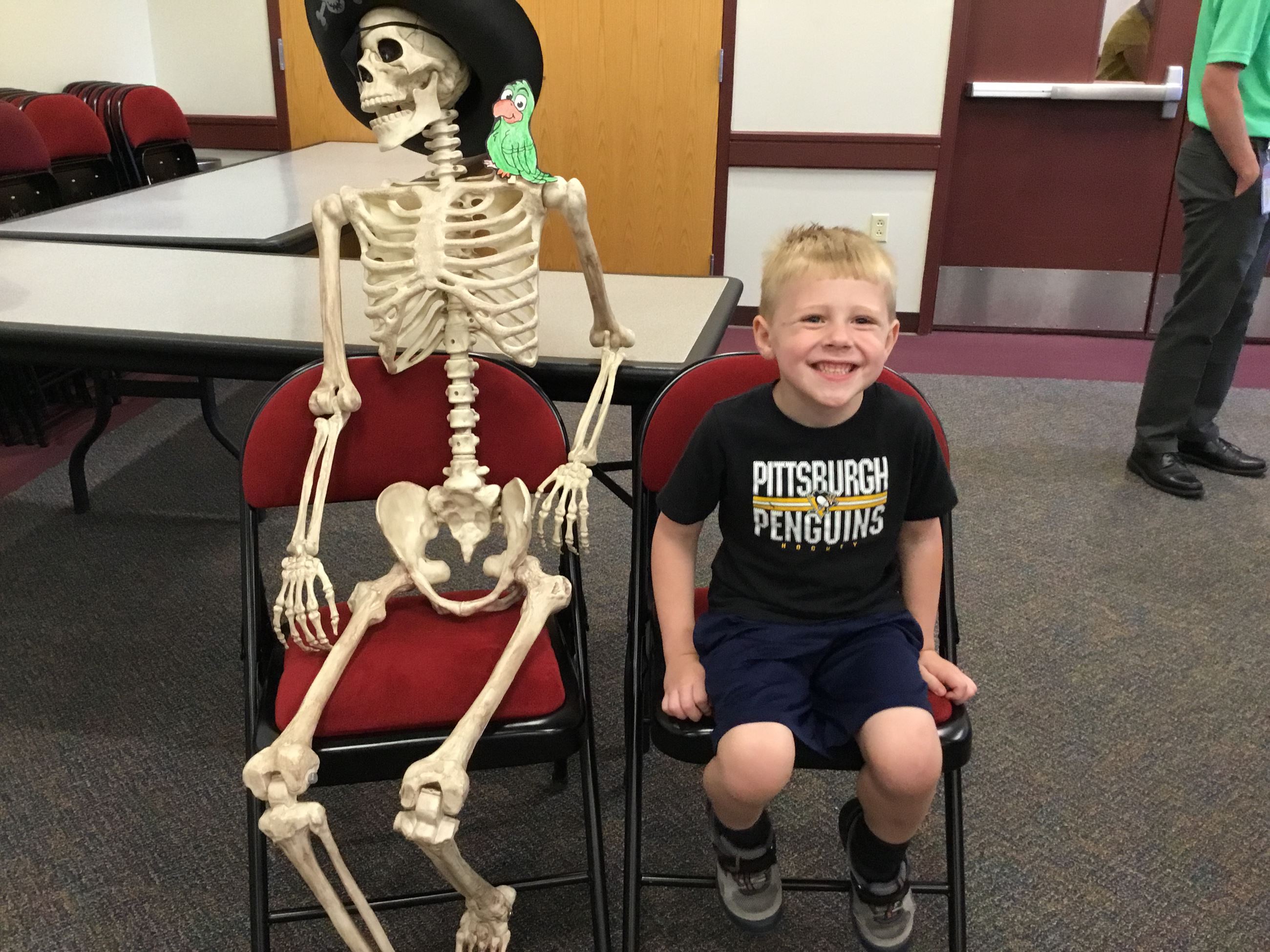 A boy sitting next to a plastic skeleton 